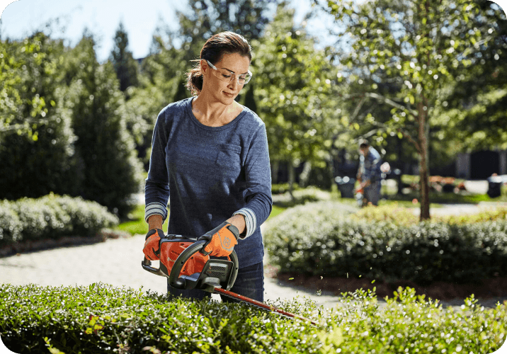 woman in backyard trimming bushes with brushcutter